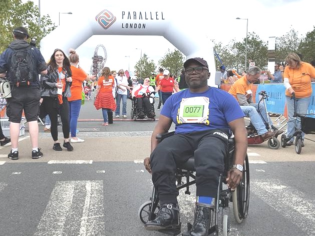 black man on wheelchair with sign of Parallel London behind him
