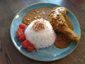 Malaysian chicken curry with onion flakes and cherry tomatoes  on a blue plate
