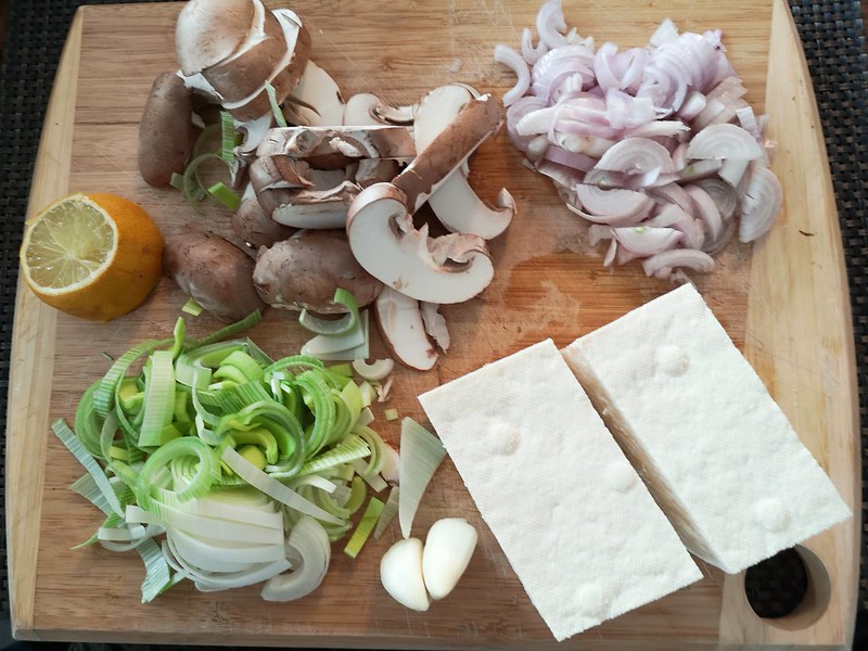 photo of cut up vegetables on choping board, with tofu, leeks, muhroom, shallots and garlic