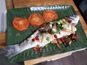Fried Seabass with tomatoes on a green banana leaf plate