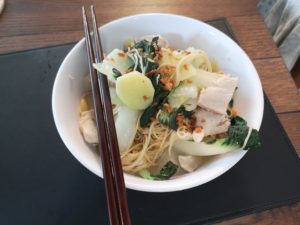 white bowl with chopsticks , noodles and green leafy vegetables